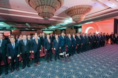 Salonda ayakta duran katılımcılar ve arkada bayrak görseli yansıtılan ekran