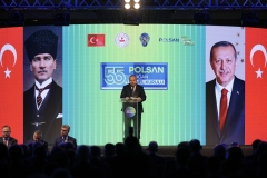 Bayrak ve portrelerle çevrili sahne ekranının önünde kürsüde konuşan konuşmacı
